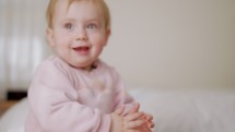 Cute baby sitting on a bed, playing, rolling and laughing
