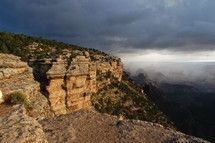 Mountain cliffs overlooking a deep canyon with dark storm clouds behind