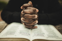 man with fingers laced in prayer over a Bible