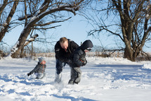 father and sons playing football in the snow 