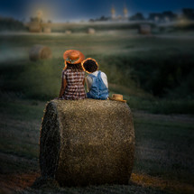 a brother and sister sitting on a hay bale 