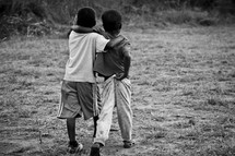 Two young boys walking together with their arms around each other