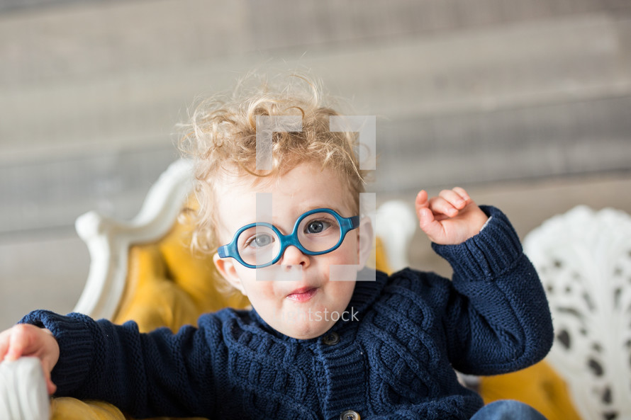 a toddler in glasses sitting on a couch 