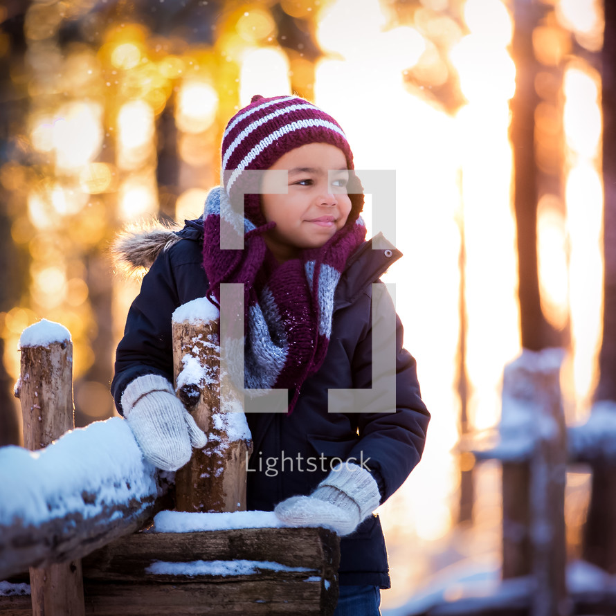 a boy leaning on a fence with snow 