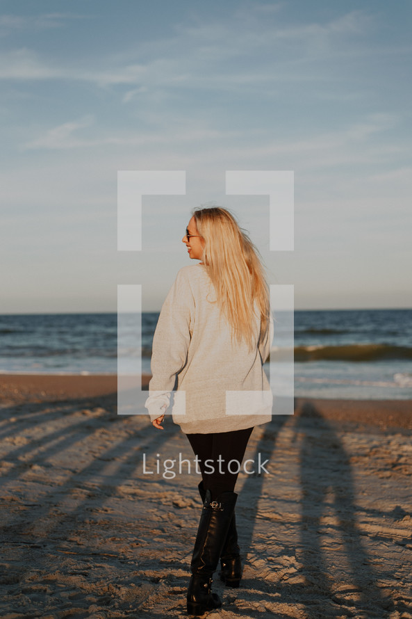 a woman walking on a beach in boots 