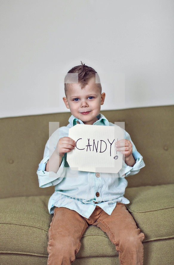 A boy child holding a sign that reads Candy