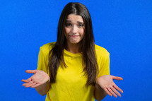 Guilty confused woman making oops, im sorry expression. Girl with long hair is ashamed and feeling uncomfortable because of guilt. Blue studio background. High quality photo