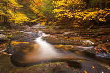Waterfall cascade in Welton Falls, New Hampshire flowing over rocks with slow shutter speed in the woods with autumn foliage