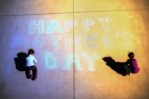 Young girls making a Mother's Day message in chalk on a driveway.