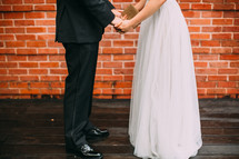 Bride and groom holding hands outside in front o a brick wall.