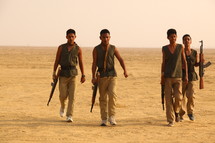 young men walking with rifles through the desert 