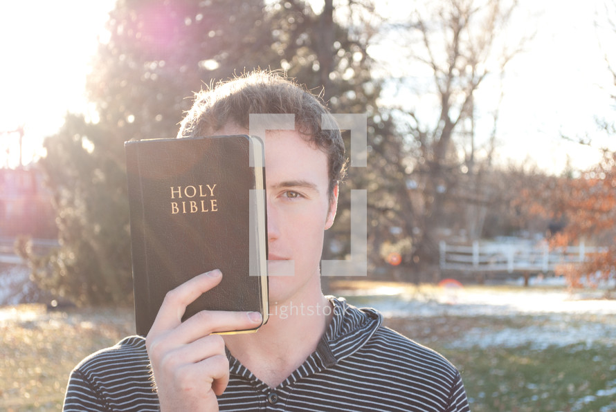 young man holding a Bible in front of half his face