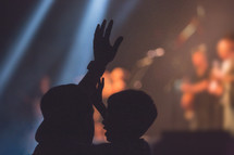 silhouette of a father and son and raised hands of an audience at a concert 