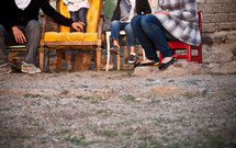 Family sitting in chairs in the dirt outside.