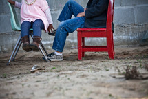 Children sitting in chairs in the dirt.