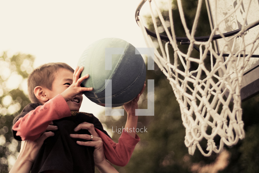 father lifting his son up to put a basketball in the net