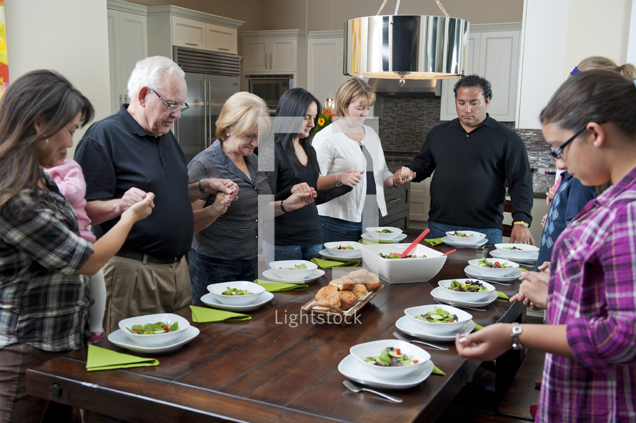 Family Saying Grace At Dinner Table