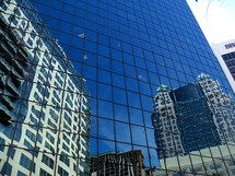 A glass building reflects the old and the  new buildings that stand side by side in a downtown city on a bright sunny day depicting commerce, business, corporate life and urban renewal city life. 