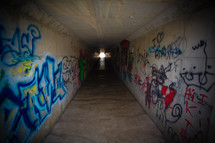 Cross light at the end of a graffiti-covered tunnel.