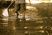 child with a net walking in a creek
