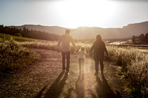 mother and father walking holding their daughters hand at sunset outdoors 