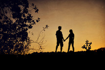 Silhouette of a couple holding hands at sunset.