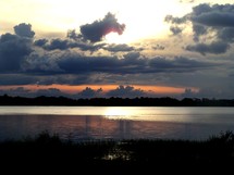 Silhouette of a treeline on the horizon with and evening sunset over cloudy skies reflecting in a calm, peaceful lake in Florida.