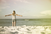 Woman with arms extended staning in the ocean waves.