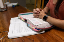 Woman's folded hands in prayer resting on open Bible during Bible study time in discipleship group