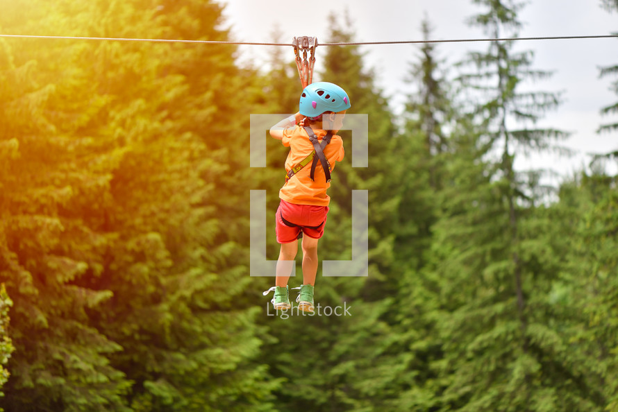 kid with helmet and harness on zip line between trees