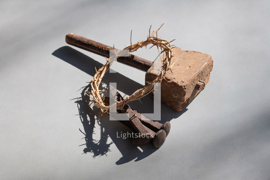 Wooden Mallet, Crown of Thorns and Three Nails with shadows on a grey background