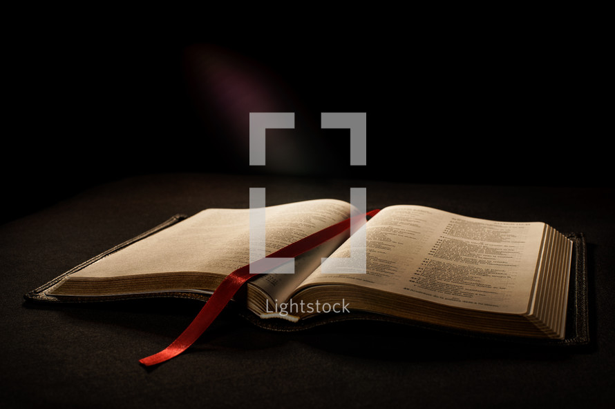Beautiful open Bible with red ribbon bookmark on pages. Warm light and black background.