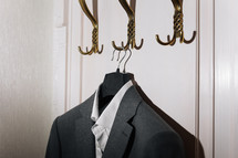Man's dark grey suit jacket and white shirt hanging on gold metal hook on white wall background