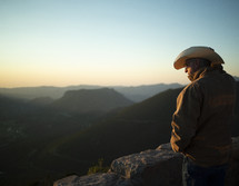 man in a cowboy hat standing at the top of a mountain 
