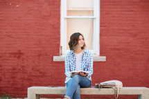 a woman sitting on a stone bench holding a Bible 