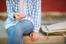 a woman sitting on a stone bench checking cellphone 