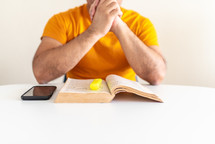 a man with praying hands reading a Bible 