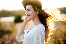 a girl in a hat with curly hair blowing in the breeze