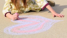 a little girl drawing a Valentine's heart on concrete with sidewalk chalk 