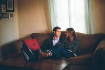 Smiling couple sitting on a sofa with their feet on a coffee table.