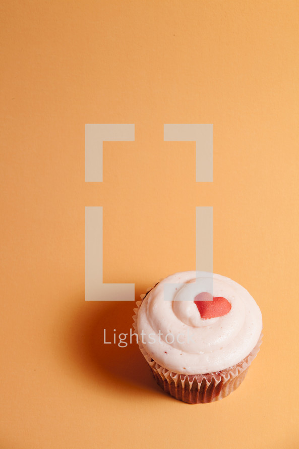 Valentine's cupcake with red heart on orange background.