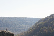 a woman standing on a edge of cliff with raised hands 
