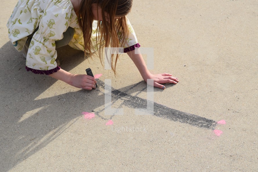 a girl child drawing a cross in sidewalk chalk 