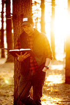 a man leaning against a tree reading a Bible 