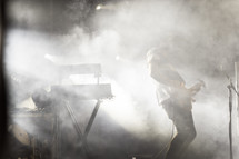 Silhouette of a musician and instruments on a foggy stage.