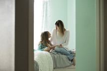 mother and daughter talking on a bed 