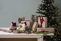 Festive Christmas Stock Photos: Presents on a Table, Some Wrapped, Some Unwrapped, Featuring a Christmas Tree in the Background and a Pristine Wall