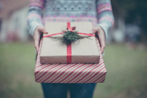 A woman in a colorful sweater holding gifts wrapped in brown and red paper
