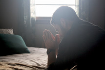 a man praying by his bedside 