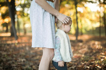 a mother and toddler daughter standing in fall leaves 